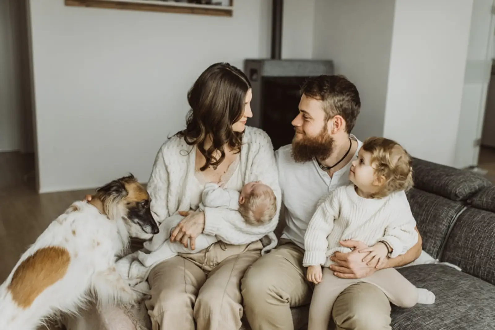 Eine Familie sitzt zusammen auf einem Sofa, umgeben von einem Hund und einem Baby.